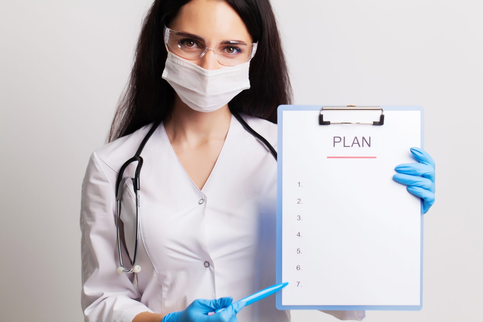 Doctor in a gloves, mask and glasses holds sheet with text plan.